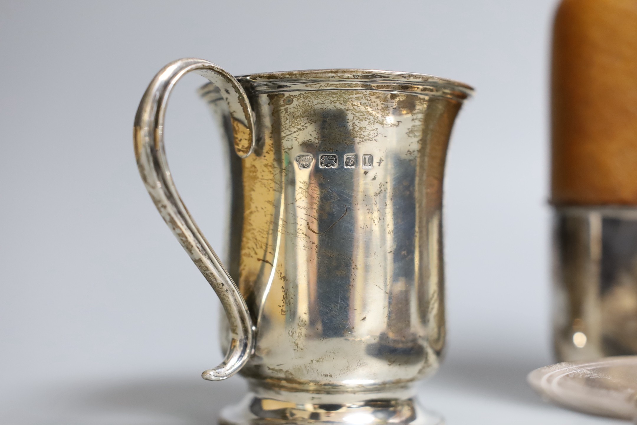 Two small George V christening mugs, a small modern silver armada dish, a silver napkin ring, ornate silver spoon and a silver plate and leather mounted glass hip flask.